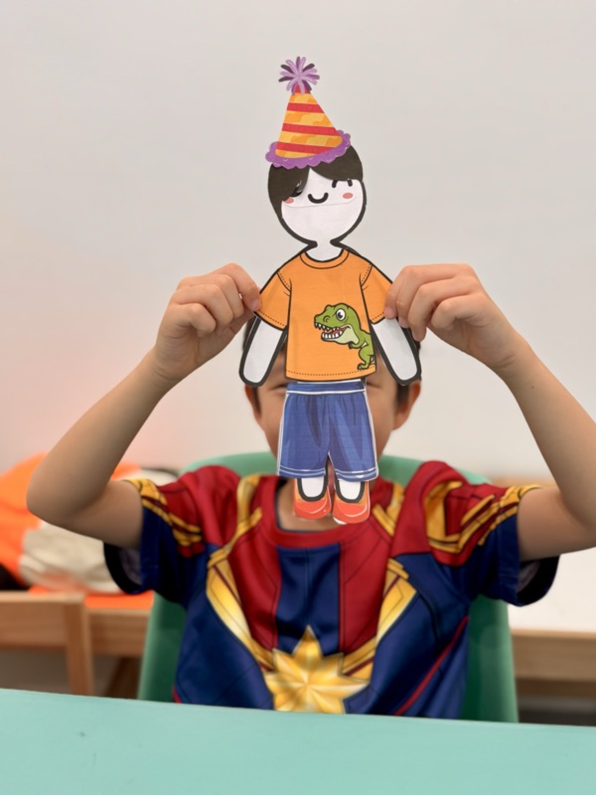 Student holding a handmade paper-doll character wearing a superhero costume