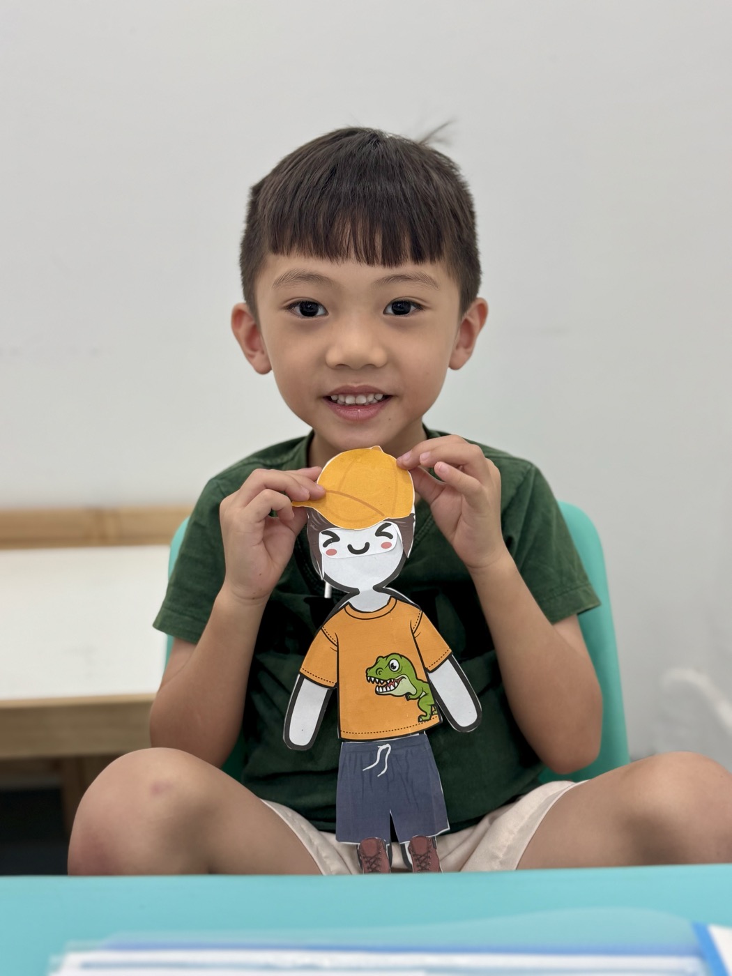 Student proudly holding his handmade paper-doll self-portrait, part of a creative writing character activity
